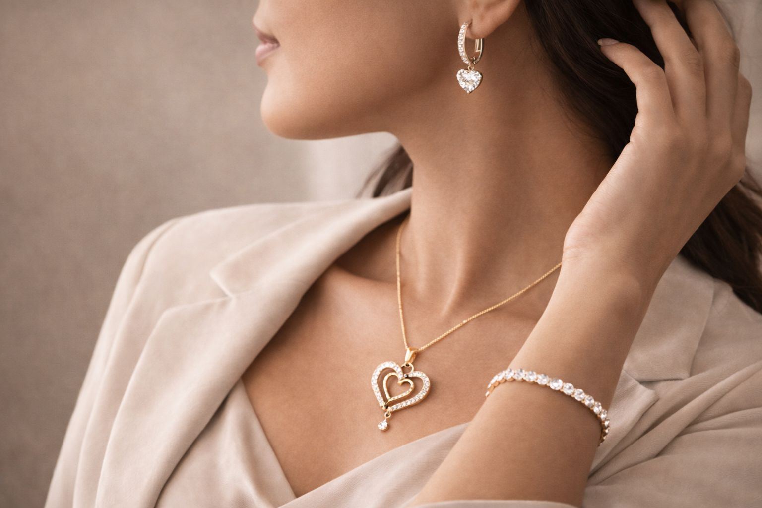 Woman wearing AuDiams's gold heart-shaped necklace, earrings, and bracelet against a neutral background side angle